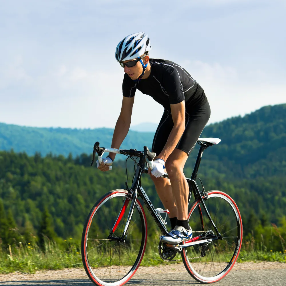 A road cyclist climbing a quiet road with forested hills behind