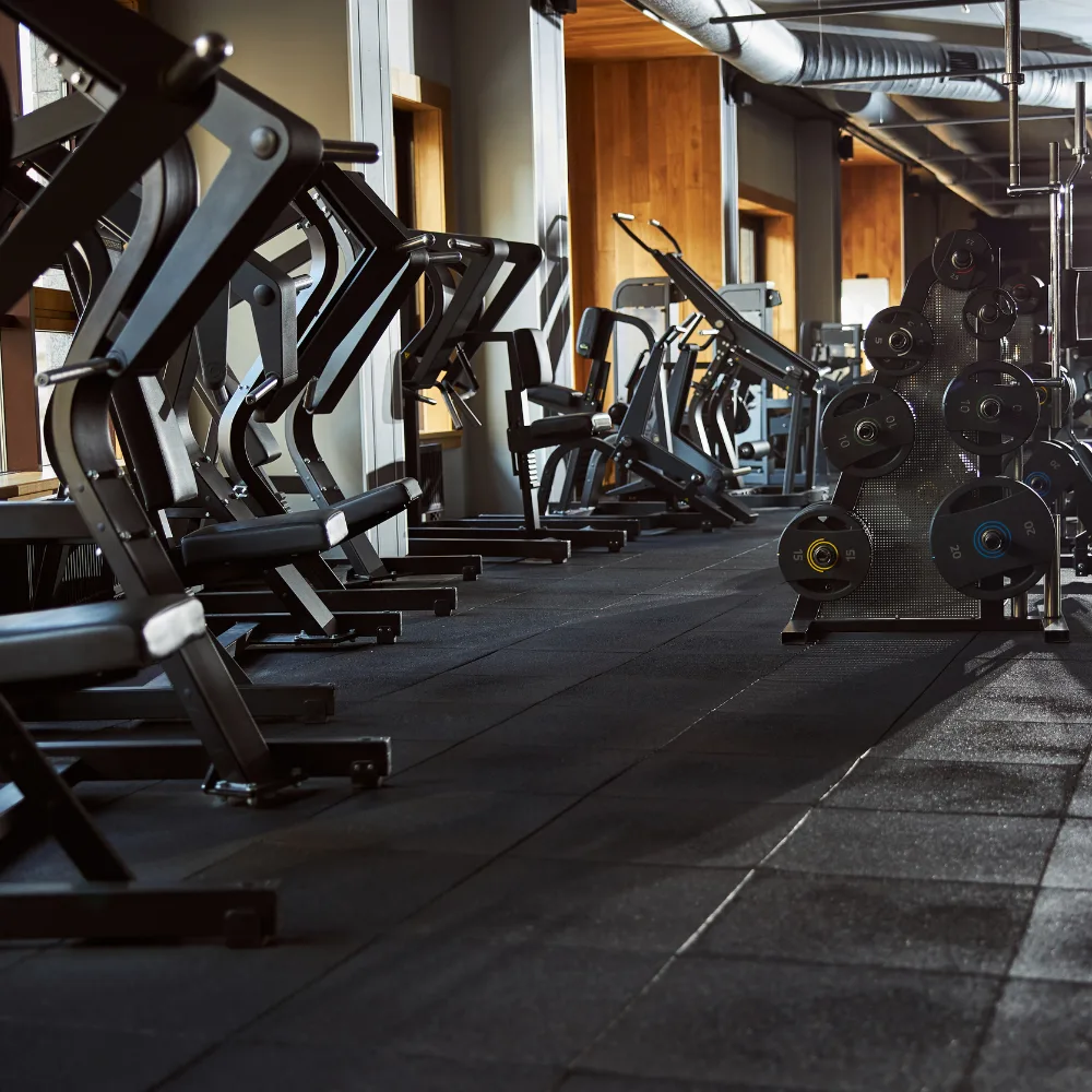 A gym floor of plate-loaded resistance machines beside a rack of weight plates