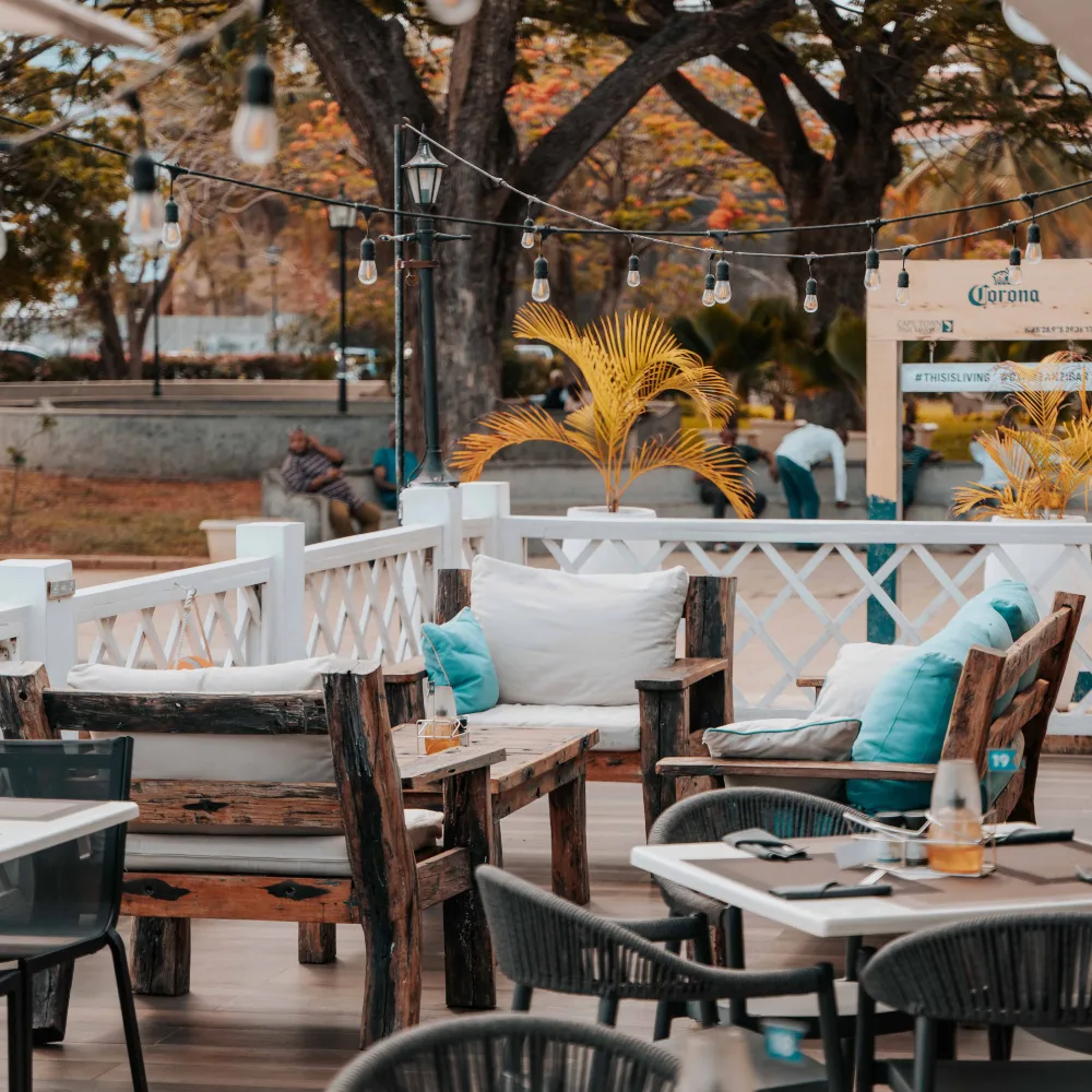 Timber armchairs and dining tables on a terrace under trees and festoon lighting